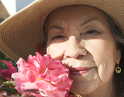 Older lady posing smiling with a red rose next to her nose
